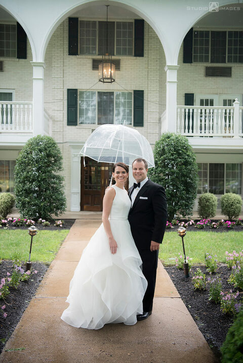 Bride and groom smiling under an umbrella on their wedding day at The Madison Hotel in Morristown. 