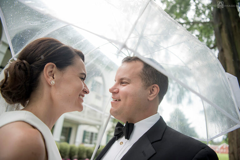 Bride and groom smiling under an umbrella on their wedding day at The Madison Hotel in Morristown. 