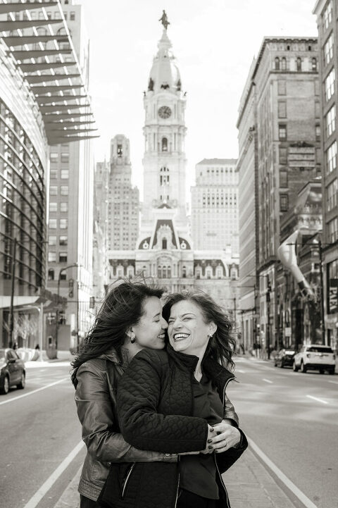 couple embracing in front of Philadelphia City Hall during their engagement session in Philly.