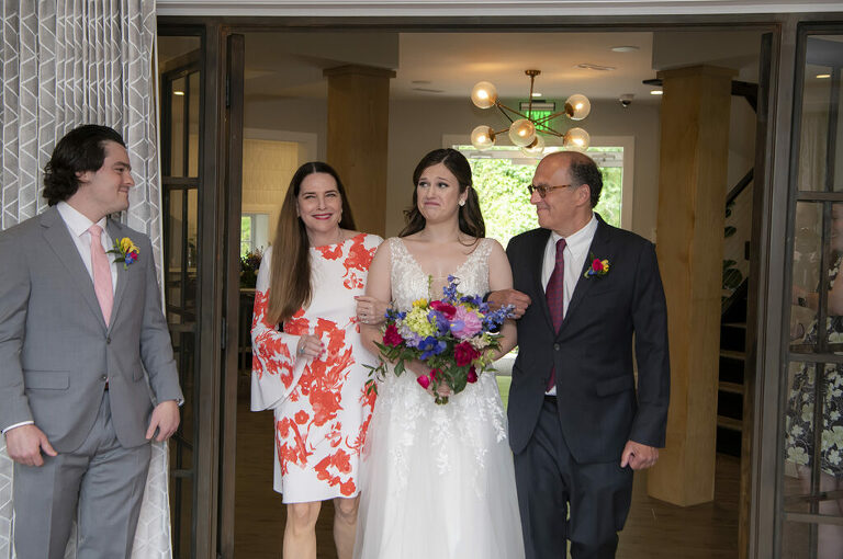 bride escorted by parents into wedding ceremony on wedding day at River House at Odette’s in New Hope.