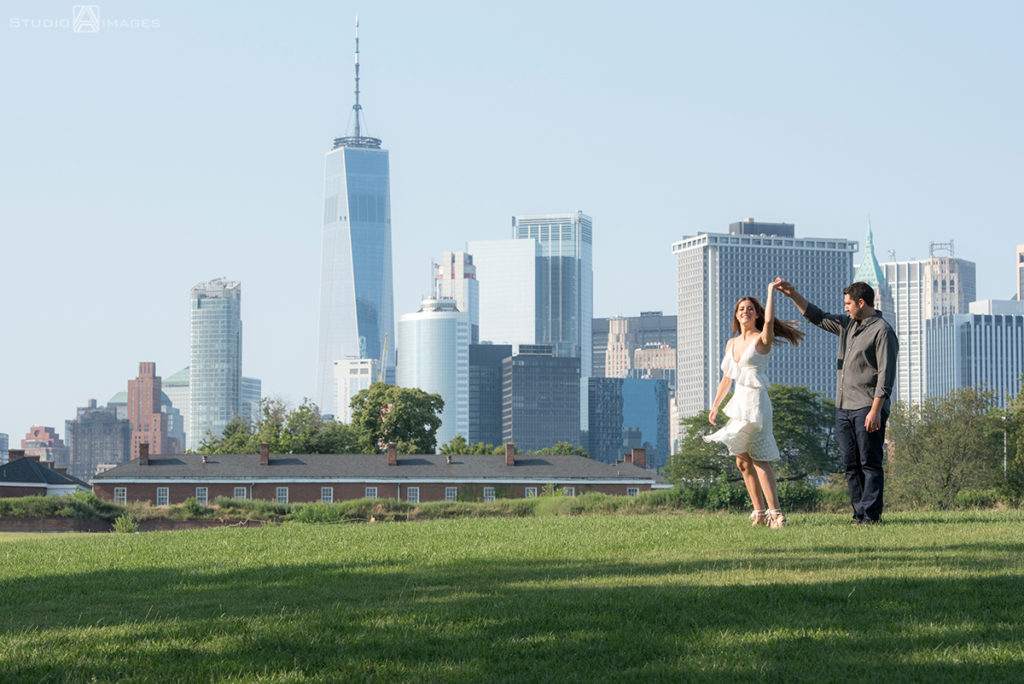 couple posing for their engagement photos at Governors Island with NYC skyline behind them